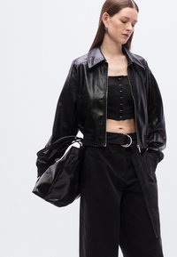 Μαύρο δερμάτινο κοντό μπουφάν με φαρδιά γιακά, εφαρμοστό επάνω μέρος με κουμπιά και φαρδιά μαύρη παντελόνα. Επιπλέον αξεσουάρ: μια μαλακή μαύρη τσάντα χειρός.