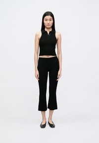 Čierny žebrovaný bezrukávový polo crop top s gombíkovým zapínaním, v kombinácii s čiernymi zvonovými nohavicami dĺžky po členky. Jednoduchý dizajn a hladká textúra.