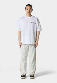 Hvit oversized t-skjorte med korte ermer, med svart tekst. Kombinert med støvete kremfargede bukser og svarte joggesko med lyse detaljer.