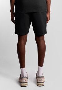 Pantaloni corti di cotone neri con vestibilità rilassata, caratterizzati da una texture liscia e orlo semplice. Abbinati a sneaker beige e calzini bianchi a crew.