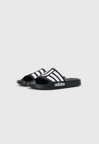 Et par sorte Adidas slides med hvide tre striber og logo på remmen, åben tå og tekstureret sål, på ensartet lys baggrund.