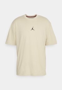 Camiseta de algodón beige con mangas cortas, cuello redondo y un pequeño logo negro de Jordan impreso en el centro. Textura suave, corte relajado.