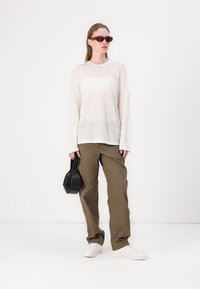 Lightweight, long-sleeve white top paired with olive green wide-leg pants. Accessories include black handbag and red sunglasses. White sneakers.