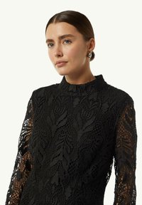 Schwarzes Spitzenkleid mit langen Ärmeln, einem hohen Ausschnitt und aufwendigen floralen Mustern mit einer strukturierten Oberfläche.