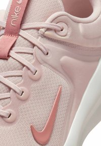 Nike urheiluvaste: vaaleanpunainen tekstiiliosa, pyöreät nauhat, kumiset yksityiskohdat, vaaleanpunainen swoosh-logo, pehmustettu nilkkapanta, sileä pohja.