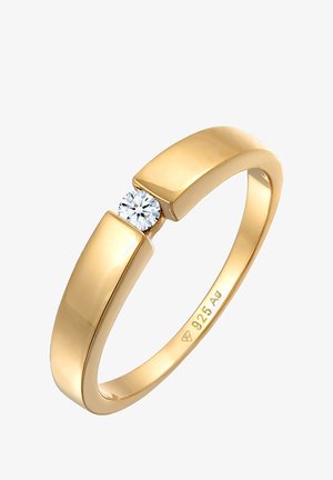 Guldfarvet ring med en glat, buet skæft og en rund klar sten, der er sat mellem to vinkelformede detaljer. Indgravering synlig indeni.