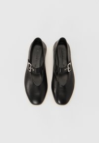 Zapatos de cuero negro con punta redonda, que presentan una correa y un detalle de hebilla de plata. Textura suave, diseño minimalista y suela plana.