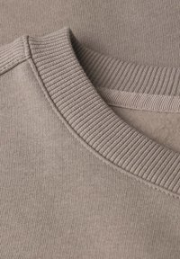 Tessuto di felpa beige, con un collo a coste e una texture liscia. Il materiale lavorato a maglia presenta un motivo uniforme e una finitura morbida.