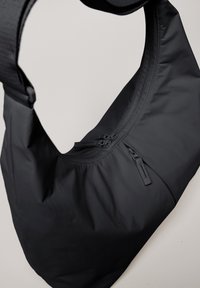 Borsa a spalla nera in tessuto con una texture liscia, dotata di una tasca con cerniera e di una tracolla larga e regolabile per un facile trasporto.