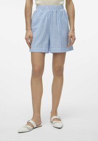 Shorts a righe blu e bianche con cintura elastica, caratterizzati da una vestibilità ampia e lunghezza fino a metà coscia. Abbinati a mule bianche intrecciate.