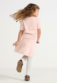 Helles rosa, flauschiges Strickkleid mit kurzen Ärmeln, einer taillierten Passform und einem ausladenden Rock. Kombiniert mit weißen Strumpfhosen und glänzenden kastanienbraunen Schuhen.
