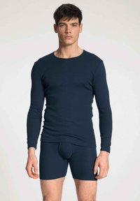 Marineblauwe langemouwen top en bijpassende slip gemaakt van ribbelsstof, met een ronde hals en een aansluitend ontwerp voor comfort en flexibiliteit.