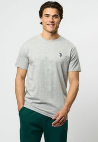 Grå bomulls t-shirt med rund hals, korta ärmar och en liten marinblå logotyp på bröstet. Pairas med mörkgröna sweatpants.
