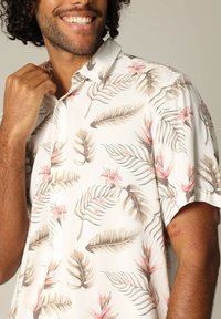 Korte mouw knoopshirt met een witte achtergrond en een bloempatroon van roze bloemen en bruine palmbladeren. Soepele stofstructuur.