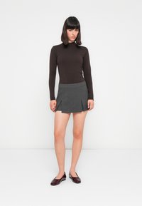 Un top lung cu mâneci lungi de culoare maro închis, asortat cu o fustă mini gri cu pliuri. Modelul poartă balerini lucioși de culoare burgundă, cu un detaliu subtil sub formă de fundă.