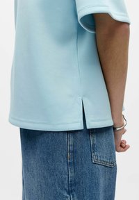 Haut bleu clair à manches courtes avec un col rond, présentant des fentes sur les côtés et une texture lisse, associé à une jupe en jean avec une poche arrière.