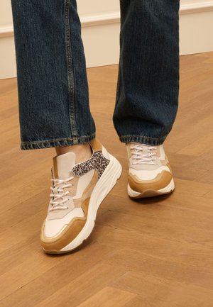 Sneakers met een beige bovenkant, beige en tan suède stukken, accenten met luipaardprint en dikke witte zolen. G gedragen met donkere denim.