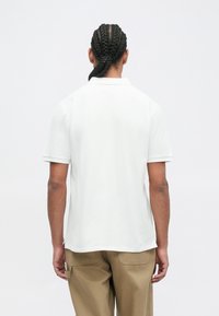 Witte polo met korte mouwen, gemaakt van een soepele stof, met een standaard kraag en subtiele stikseldetails, gedragen met lichtbruine cargobroeken.
