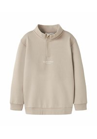 Sudadera beige con cuello de media cremallera, mangas largas y un corte relajado. Presenta el texto "Edición de estudio" en la parte frontal. Textura de tela suave.