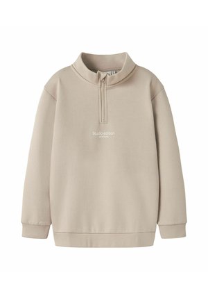 Beige sweatshirt met een halve rits kraag, lange mouwen en een relaxte pasvorm. Heeft de tekst "Studio editie" op de voorkant. Zachte stoftextuur.