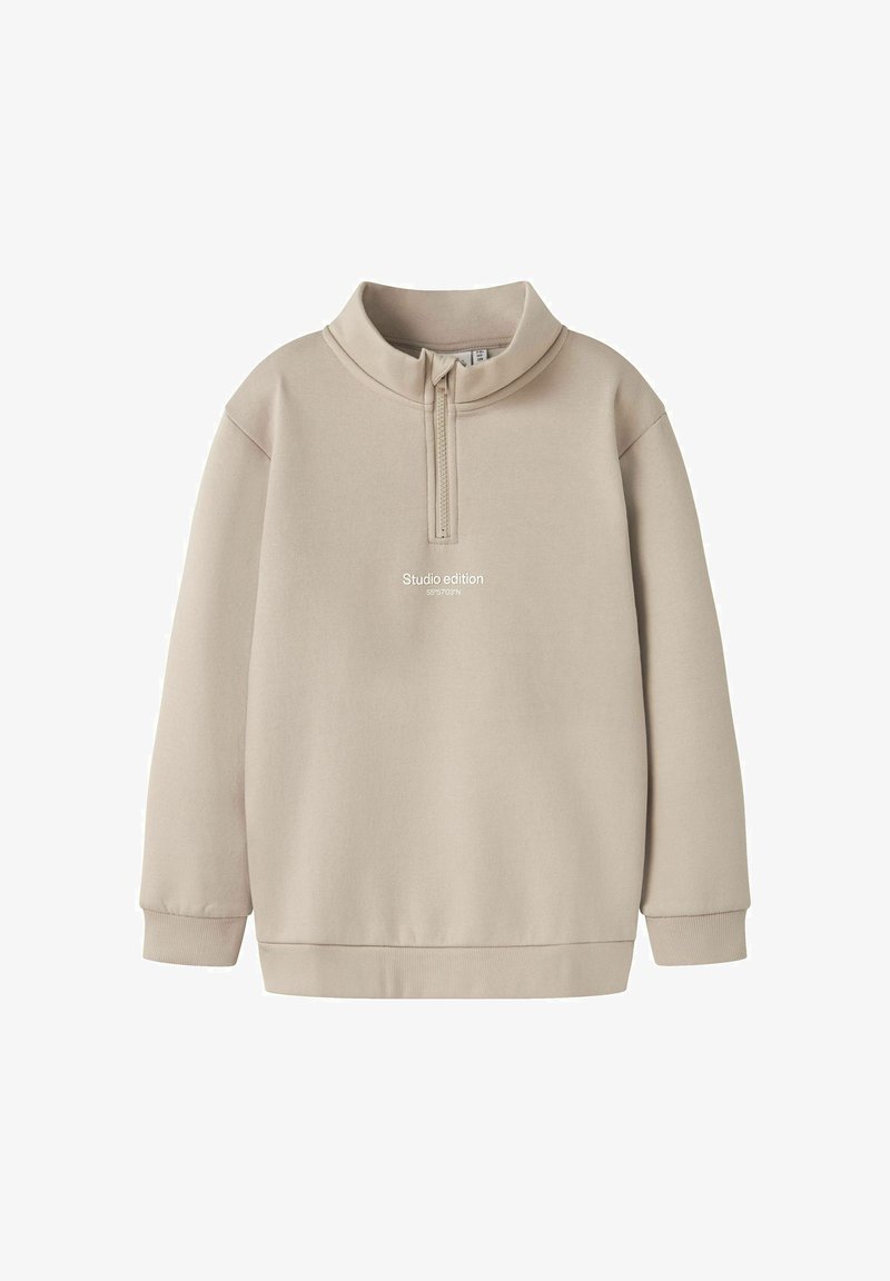 Beige mikina s půlzipem, dlouhými rukávy a volným střihem. Na přední straně je nápis "Studio edition". Měkká textilie.
