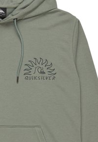 Light green hooded sweatshirt made of soft fabric. Features a dark logo with wave and sun design on the chest. Kangaroo pocket style.