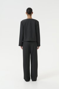 Svart skreddersydd drakt med en kort blazer og vide bukser. Glatt stoff, minimalistisk design og skjult glidelåsdetaill bak.