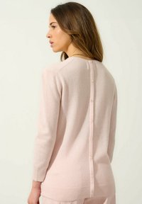 Miękki różowy sweter z dzianiny z prążkowanym wykończeniem i długimi rękawami, z zapięciem na guziki z tyłu oraz gładką fakturą.