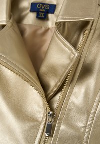 Goldfarbene Kunstlederjacke mit glatter Textur, ausgestattet mit einem Reißverschluss und einem spitzen Kragen, gekennzeichnet als OVS Kids, Größe 4-6.