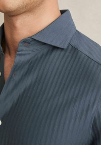 Camisa con cuello en azul oscuro con un patrón texturizado y de rayas. La tela es ligera, cuenta con un cierre de botones y un acabado suave.