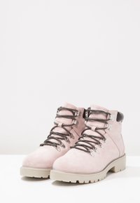 Botas de ante rosa con cordones grises y detalles en plata. Suela gruesa y tobillos acolchados para mayor soporte. Presenta una puntera redondeada y un talón reforzado.