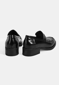 Schwarze Lederloafers mit glänzender Oberfläche, niedrigem Absatz, gestickten Akzenten und einer weichen Innenausstattung für zusätzlichen Komfort.