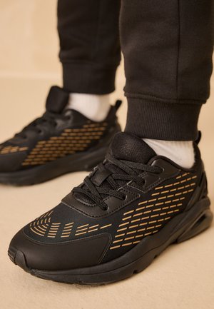 Schwarze Sportschuhe mit einem gemusterten goldenen Design. Hergestellt aus synthetischen Materialien, mit einer strukturierten Oberseite und einer Gummisohle.