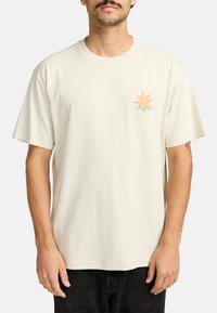 Crèmekleurig katoenen t-shirt met korte mouwen en een ronde hals, voorzien van een multikleuren zonafbeelding op de linkerborst.