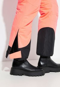 Roze en zwarte waterdichte broek met zijritsen en zakken, gecombineerd met zwarte chunky enkelaarsen, met een soepele leren textuur.
