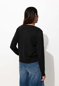 Pull noir à manches longues avec un col rond, un ourlet côtelé et une texture douce, porté avec un jean en denim bleu taille haute.