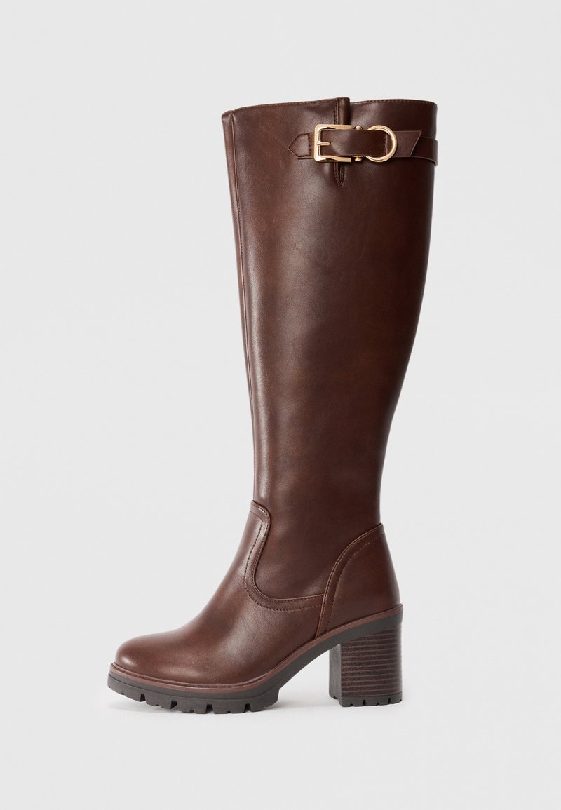 Bottes en cuir marron montant jusqu'au genou avec un large talon, dotées d'une boucle dorée et d'une semelle texturée pour une meilleure adhérence.
