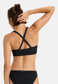 Black bikini set featuring a cross-back design with thin straps and a seamless band. The bottom has a low-rise cut with a logo detail.