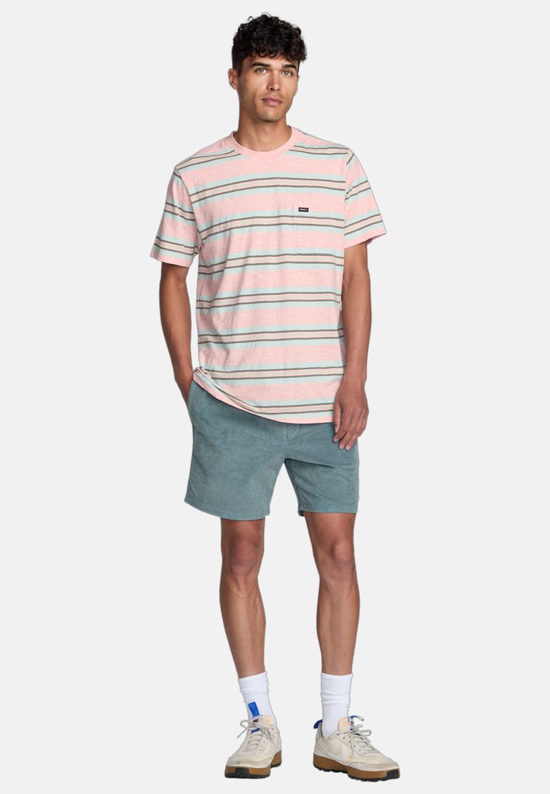 T-shirt en coton rayé rose, vert et bleu, avec des manches courtes et une poche sur la poitrine. Associé à un short bleu clair et des baskets.