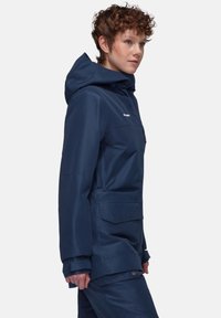 Marineblauer wasserdichter Jacke mit Kapuze, mehreren Taschen, elastischen Bündchen und einer glatten, matten Oberfläche.