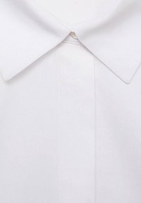 Chemise blanche à col classique, présentant une texture de tissu lisse, un design de col traditionnel et une fermeture centrale à boutons, avec des détails cousus sur la patte de boutonnage.