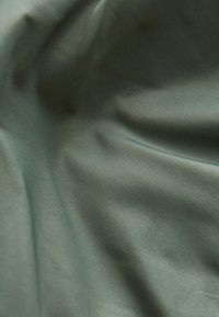 Tissu doux gris verdâtre avec une texture fine et des plis délicats créant des ombres et des reflets doux.
