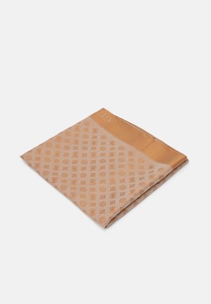 Foldet beige og brun mønstret stof med geometriske og cirkulære motiver på en ensfarvet lys grå baggrund.