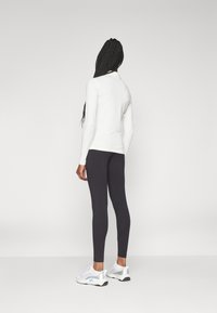 Fehér, hosszú ujjú felső fekete leggings-szel és fehér sportcipőkkel párosítva. A felső kerek nyakú; a leggings testhezálló.