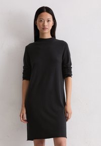 Schwarzes, langärmliges Kleid mit hohem Kragen und bequemem Schnitt aus weichem Stoff. Es verfügt über aufgerollte Ärmel und einen geraden Schnitt bis zum Saum.