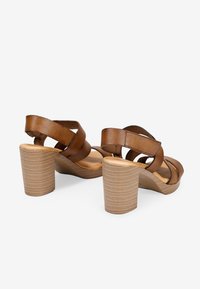 Sandalias de tacón abiertas de cuero marrón con correas entrelazadas y un tacón grueso de textura similar a la madera. Interior suave con un acabado blando.