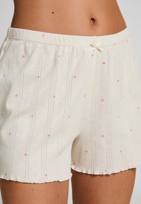 Λευκά βαμβακερά σορτς με υφή, που διαθέτουν κάθετες ρίγες και μικρές ροζ καρδούλες. Ολοκληρώνονται με ένα διακοσμητικό φιόγκο στη μέση.