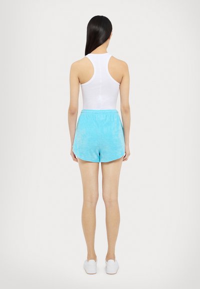 Débardeur blanc à dos nageur associé à un short tie-dye bleu clair avec une taille élastique, coupe au-dessus du genou et texture douce.