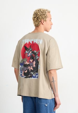 Camiseta beige de gran tamaño con un gran estampado gráfico que presenta un sol rojo, olas y figuras en acción, hecha de material de algodón suave.
