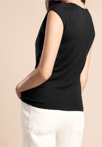 Svart ärmlös topp med en slät yta, med rund halsringning och subtila sömmar; matchas med vita byxor.